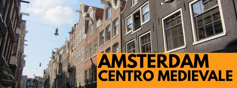 Fotografia di alcuni edifici del centro storico di Amsterdam in una giornata serena con rettangolo arancione in basso a destra con scritta nera Amsterdam Centro Medievale