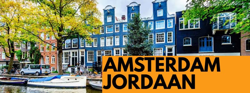 Fotografia del quartiere Jordaan di Amsterdam con alcuni edifici blu ed alberi. In primo piano c'è un canale con delle barche. In basso a sinistra rettangolo arancione con scritta nera Amsterdam Jordaan